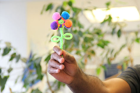 Hand holding a colourful flower made from pipe cleaners.