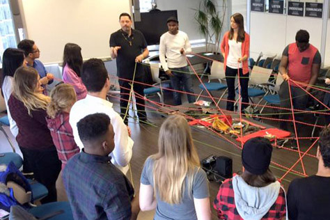  A circle of people holding colourful string that is passed from one person to another connecting everyone.